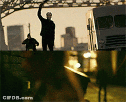 Man In Mask On Bridge With Hand Up GIF
