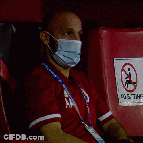 Man In Mask Sitting On Red Chair With No Sitting Sign GIF