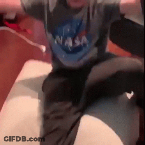 Man In NASA Shirt And Black Shorts Sitting On Bed GIF