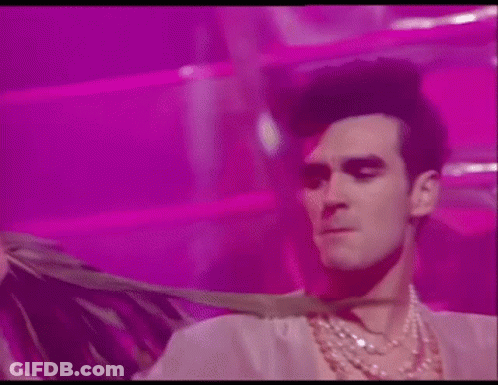 Man In Necklace And Wig Dancing On Pink Background GIF