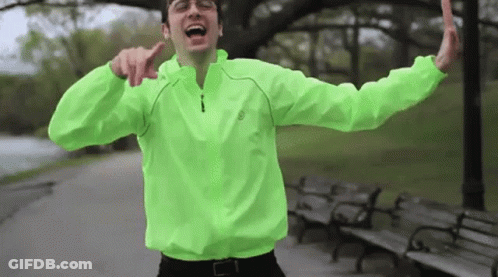 Man In Neon Green Jacket With Arms Outstretched In Park GIF