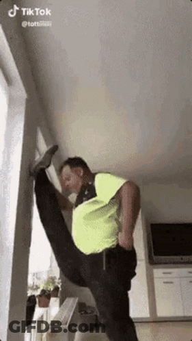 Man In Neon Green Shirt Doing Split In Living Room GIF