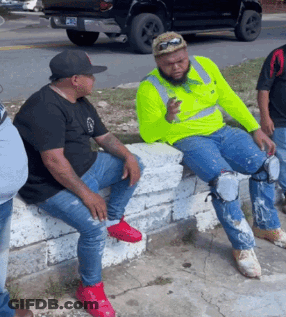 Man In Neon Yellow Shirt Sitting On Wall With Legs Crossed GIF