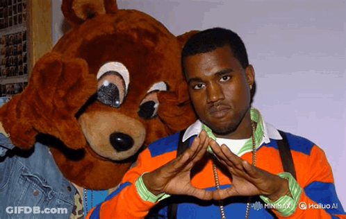 Man In Orange And Blue Sweater Next To Teddy Bear GIF