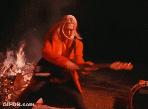Man In Orange Coat Playing Guitar By Fire GIF