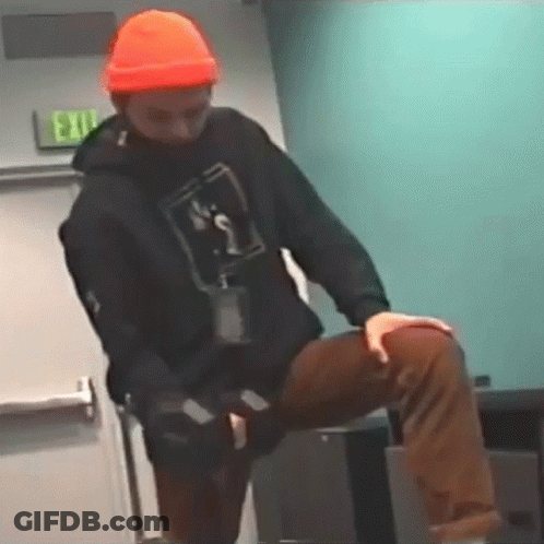 Man In Orange Hat And Black Hoodie Kneeling On Table GIF
