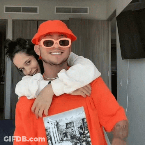 Man In Orange Hat And Sunglasses Carrying Woman On Back GIF