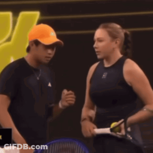 Man In Orange Hat Talking To Woman With Tennis Racquet GIF