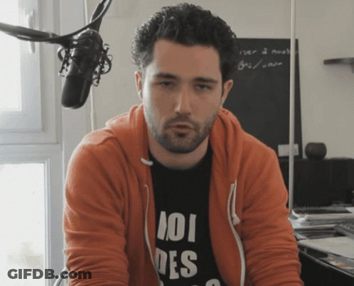 Man In Orange Hoodie And 101 Des Shirt At Microphone GIF