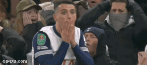 Man In Orange Hoodie And White Jacket Looking At Camera GIF