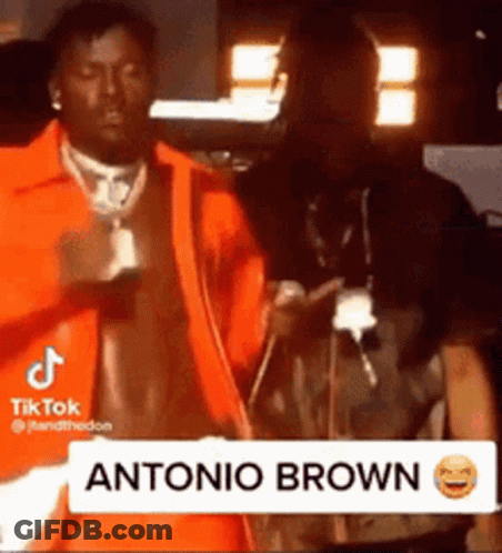 Man In Orange Jacket Next To Man In Dark Room GIF