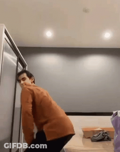 Man In Orange Jacket Standing In Front Of Refrigerator GIF