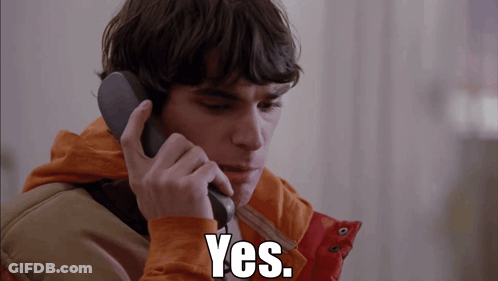 Man In Orange Jacket Talking On Phone Saying Yes GIF