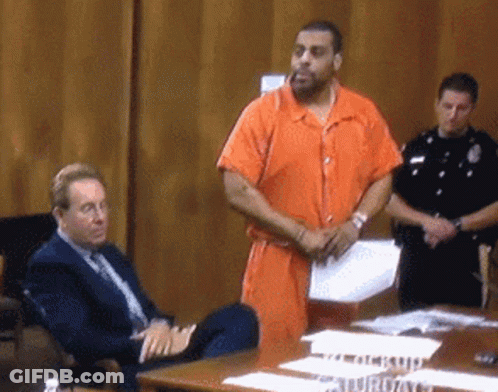 Man In Orange Jumpsuit Standing Before Man In Suit At Table GIF