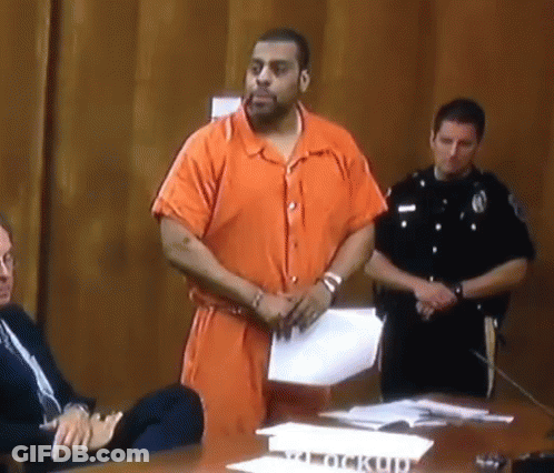 Man In Orange Jumpsuit Standing By Clock Up Sign GIF