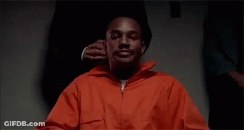 Man In Orange Prison Uniform Sitting With Man Holding His Ear GIF