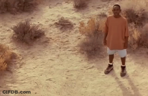Man In Orange Shirt And White Shorts Standing In Dirt Field GIF
