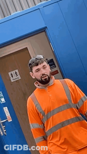 Man In Orange Shirt By Blue Door Saying Toilets GIF