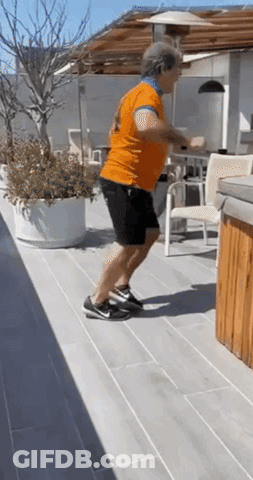 Man In Orange Shirt Doing Squats On Patio GIF