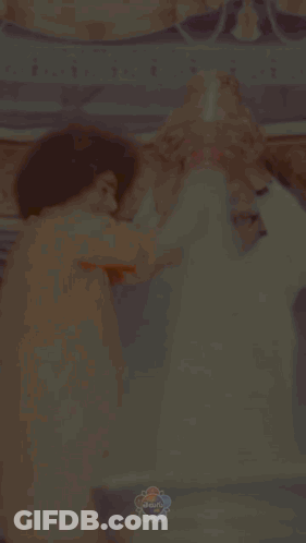 Man In Orange Shirt Holds Bell Over Man In White Shirt GIF