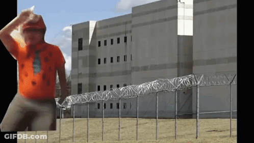 Man In Orange Shirt In Front Of Barbed Wire GIF
