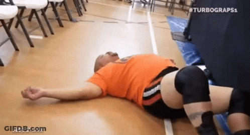 Man In Orange Shirt Lying In Wrestling Ring GIF