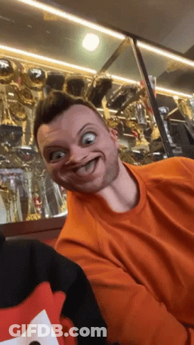 Man In Orange Shirt Making Funny Face With Trophies GIF