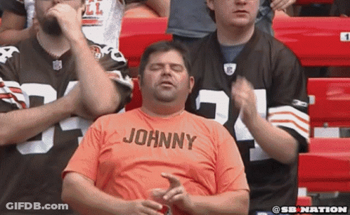 Man In Orange Shirt Saying Johnny Sitting In Stadium GIF