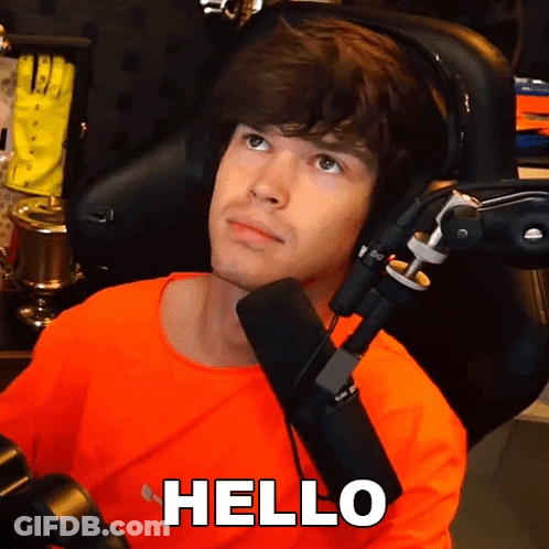 Man In Orange Shirt Sitting In Front Of Microphone With Hello Above Head GIF