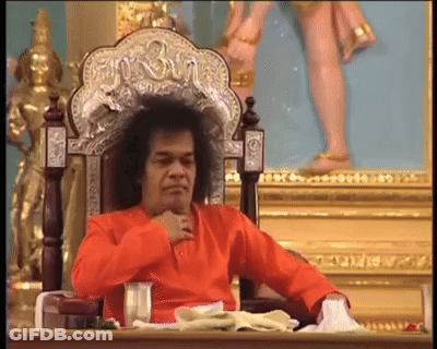 Man In Orange Shirt Sitting With Shree Statue GIF