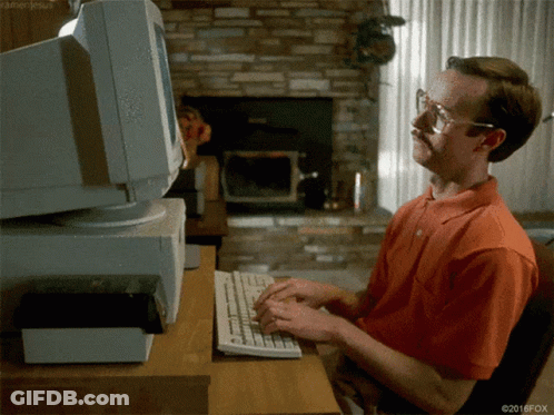 Man In Orange Shirt Typing At Computer GIF