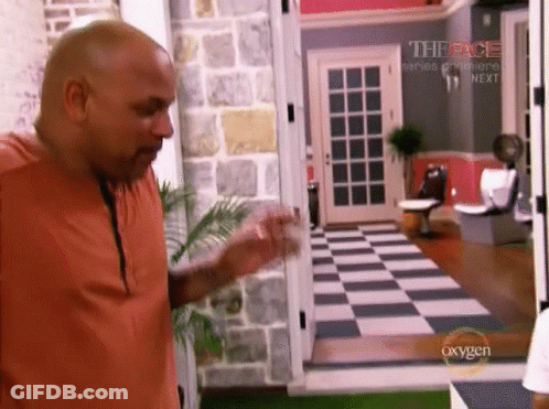 Man In Orange Shirt With Peace Series Premiere Sign On Checkered Floor GIF