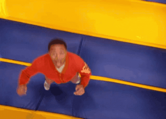 Man In Orange Sweater Bouncing Inflatable Playground GIF