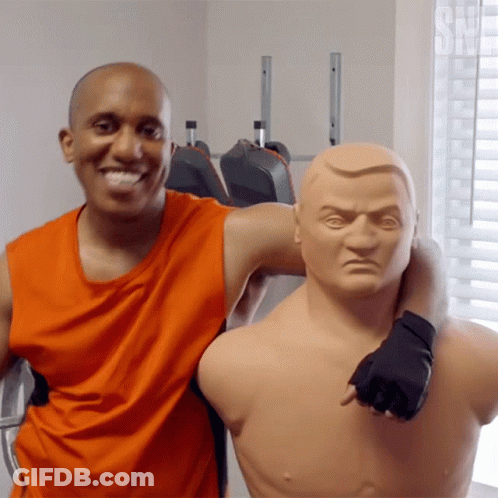 Man In Orange Tank Top Posing With Boxing Mannequin GIF