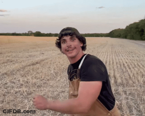 Man In Overalls And Black Shirt Smiling In Field GIF