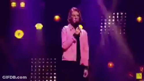 Man In Pink Jacket Holding Microphone On Stage GIF