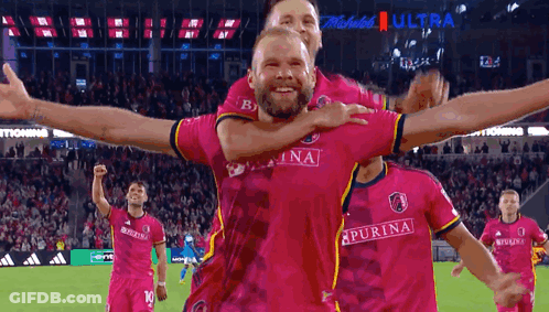 Man In Pink Purina Jersey Being Lifted By Another Man GIF