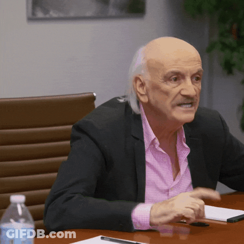 Man In Pink Shirt And Black Jacket Sitting At Table GIF