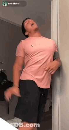 Man In Pink Shirt And Black Shorts Leaning Against Wall GIF
