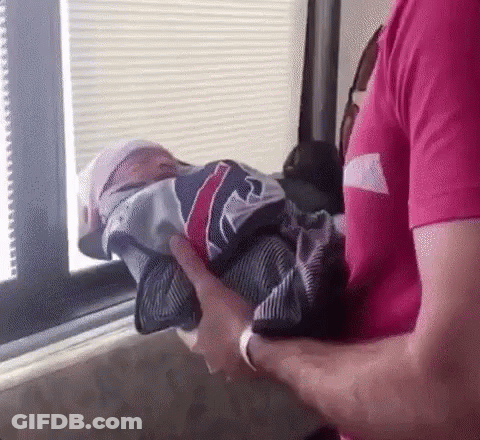 Man In Pink Shirt Holding Baby Wrapped In Jersey GIF