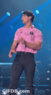 Man In Pink Shirt Singing Into Microphone On Stage GIF