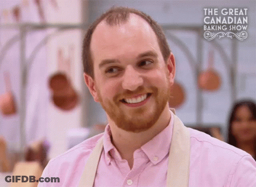 Man In Pink Shirt Smiling In Front Of Baking Show Sign GIF