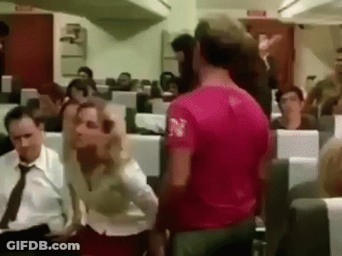 Man In Pink Shirt Standing In Front Of Group On Airplane GIF