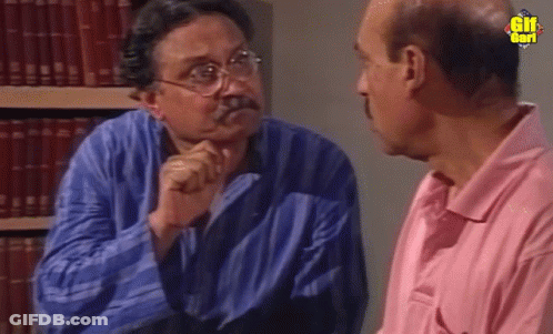 Man In Pink Shirt Talks To Man In Library GIF