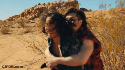 Man In Plaid Shirt Carrying Woman In Desert GIF