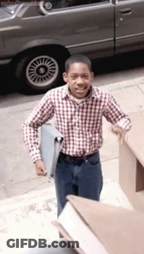 Man In Plaid Shirt Holding Box In Front Of Car GIF