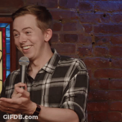 Man In Plaid Shirt Holding Microphone In Front Of Stained Glass Window GIF