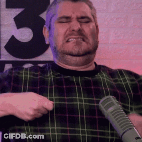 Man In Plaid Shirt Holding Microphone In Front Of Wall Number 3 GIF
