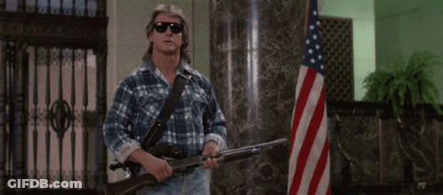Man In Plaid Shirt Holding Two Guns In Front Of American Flag GIF