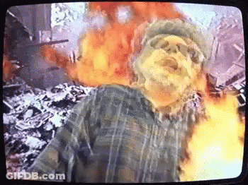 Man In Plaid Shirt In Front Of Fire Explosion On TV GIF